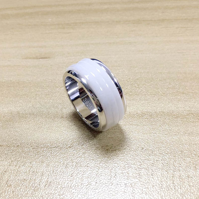 Silver ring with a white ceramic band on a beige surface