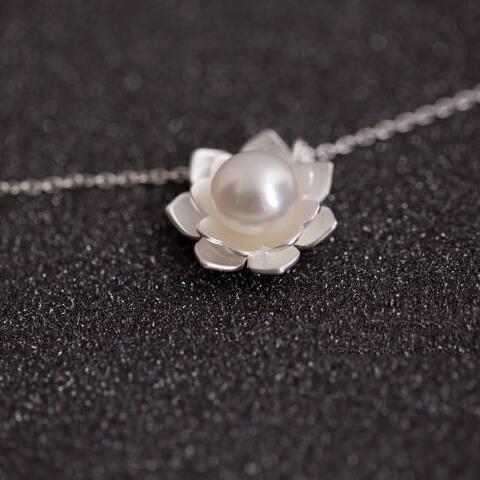 Silver necklace with a lotus flower pendant featuring a pearl on a dark textured background