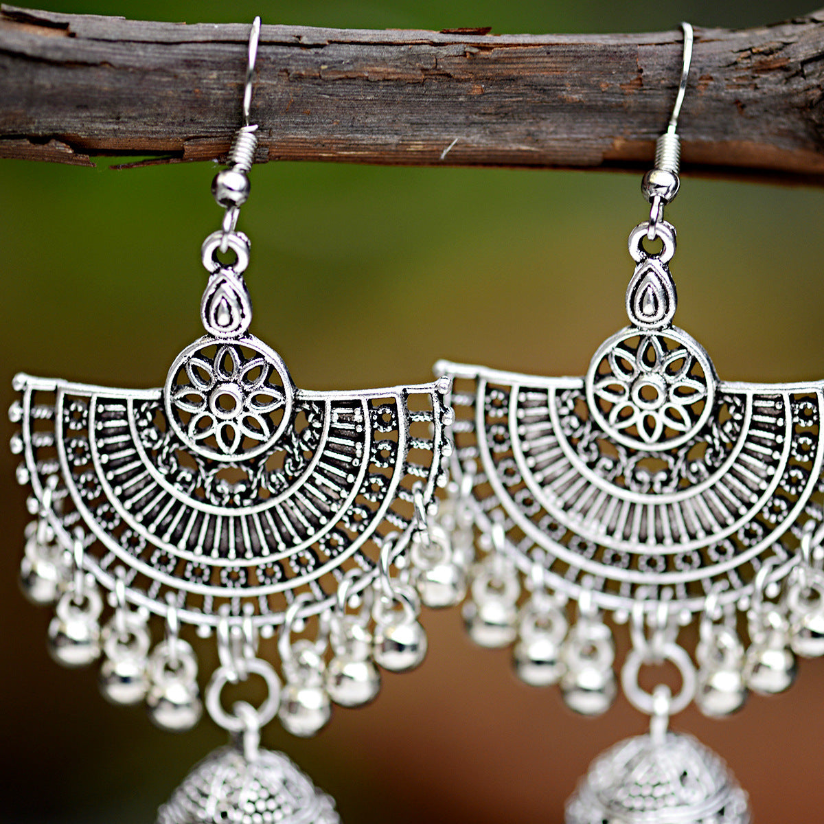 Silver earrings with intricate designs hanging from a branch.