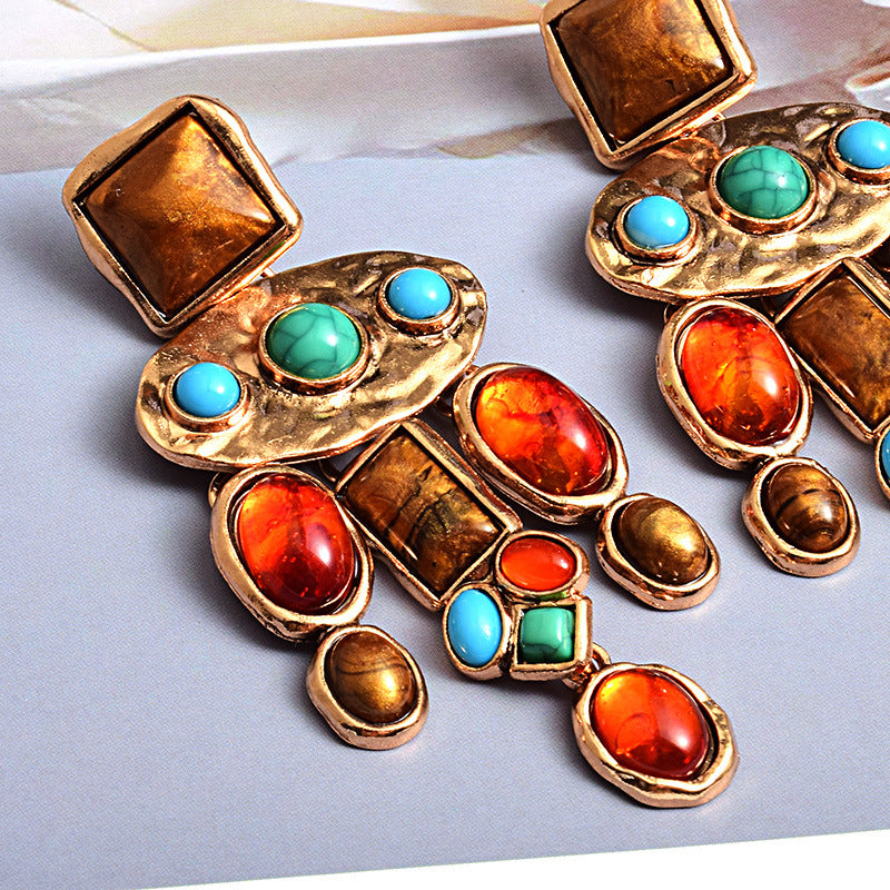 Gold earrings with colorful gemstones on a light gray background