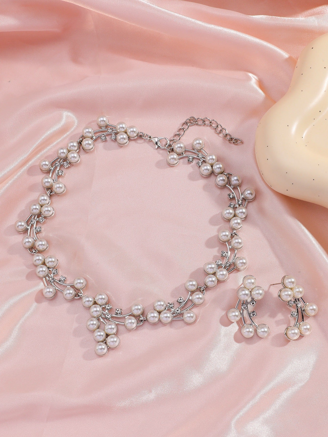 Pearl necklace and earrings on a pink fabric background