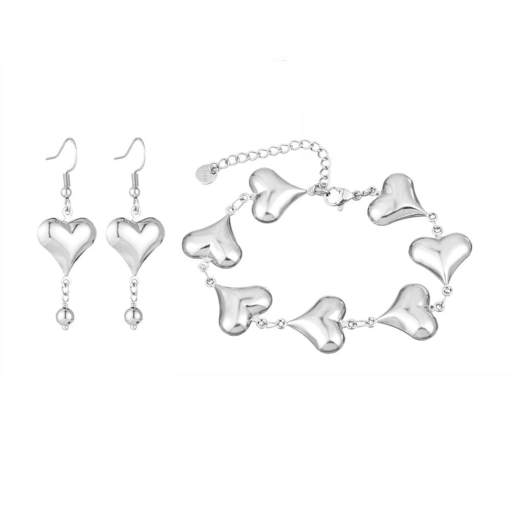 Silver heart-shaped bracelet and earrings on a white background