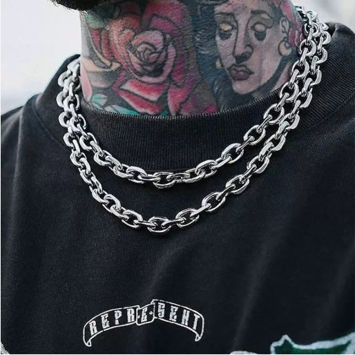Person wearing a black hoodie with a chain necklace and visible tattoos.