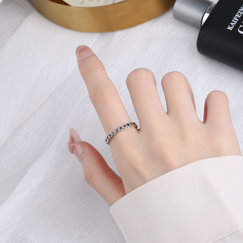 Hand wearing a silver ring with small stones on a white surface