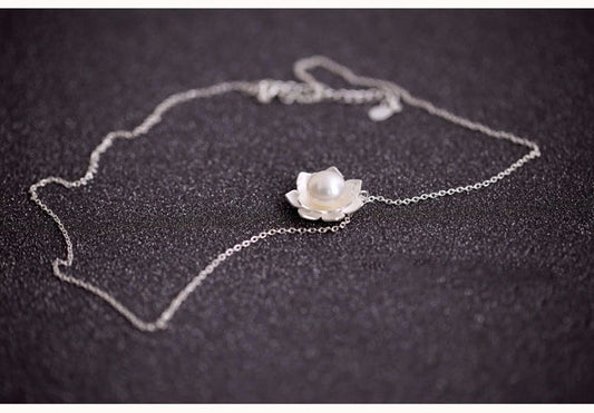 Silver necklace with a flower-shaped pendant on a dark surface
