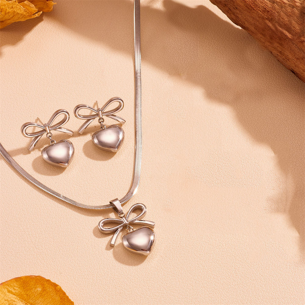 Silver necklace with heart and bow pendants on a beige background