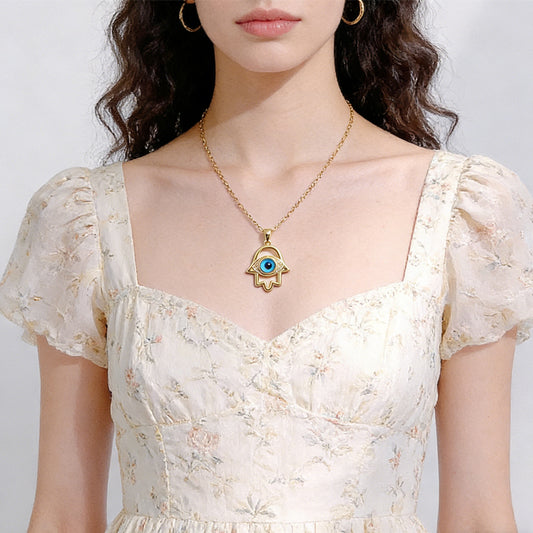 Woman wearing a gold necklace with a blue eye pendant on a plain background