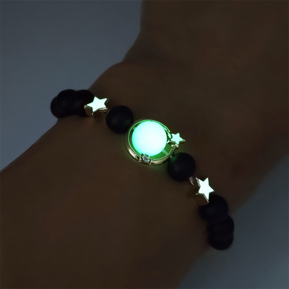 Glowing bracelet with black beads and star-shaped ends on a wrist against a dark background