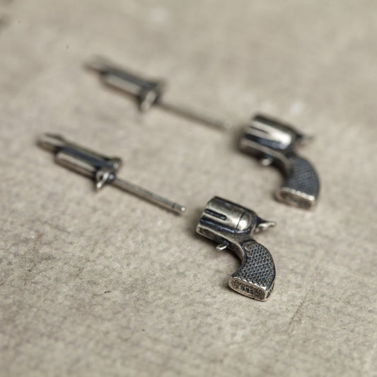 Silver gun-shaped earrings on a textured beige surface