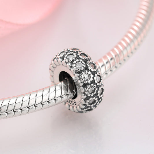 Silver charm with embedded stones on a pink background