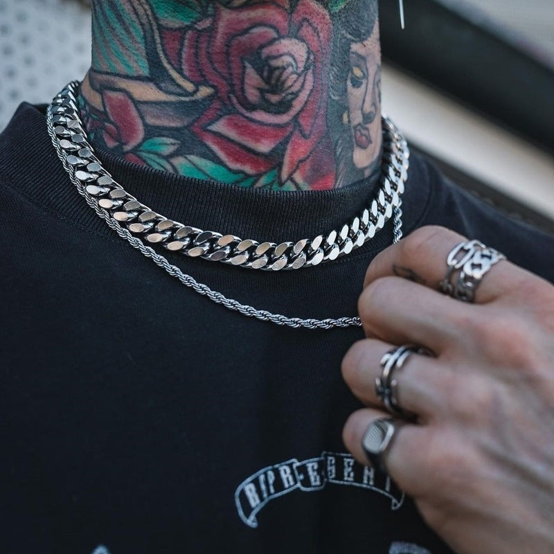 Person wearing multiple silver chains and rings with tattoos on neck and chest.