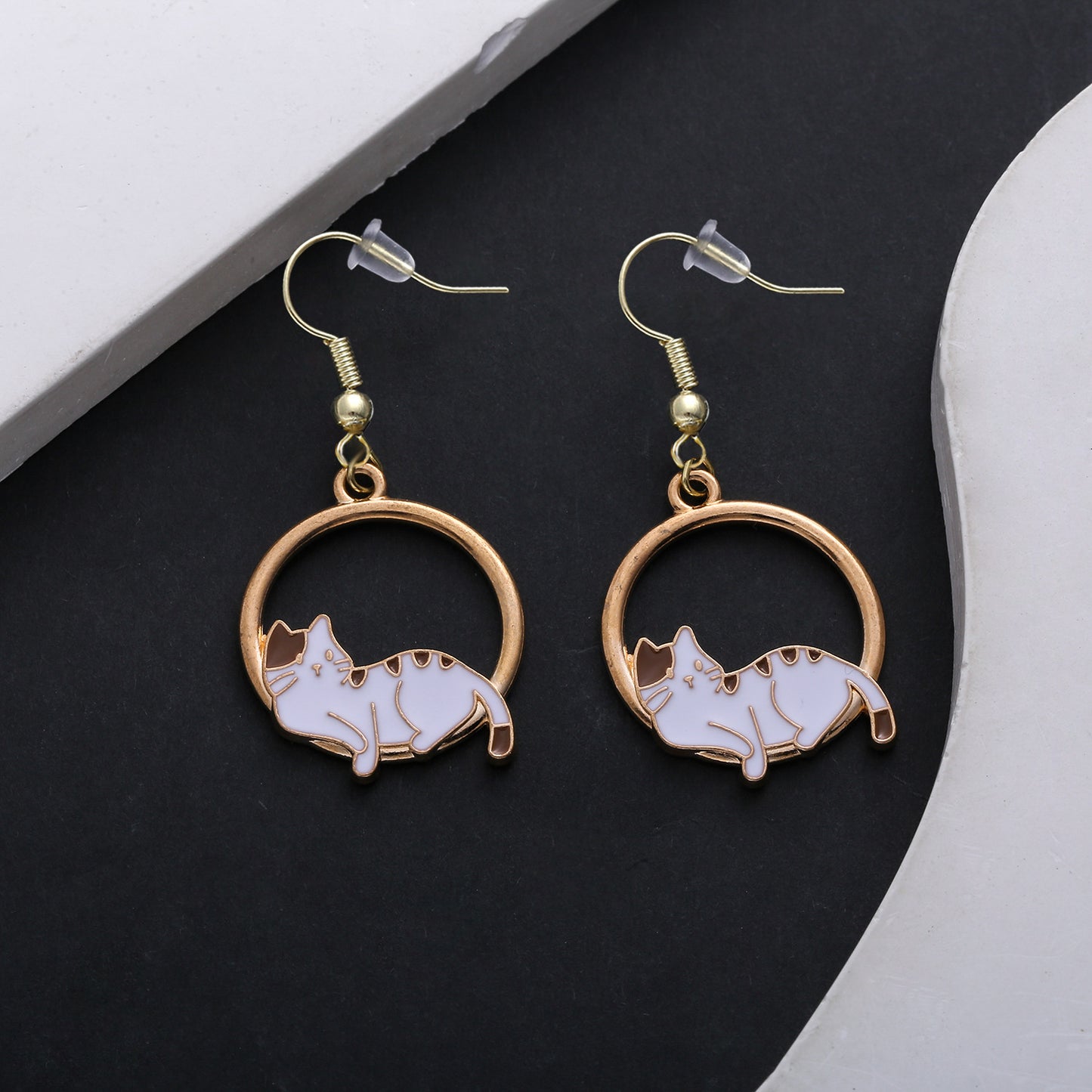 Cat-shaped earrings with gold circular frames on a dark surface.