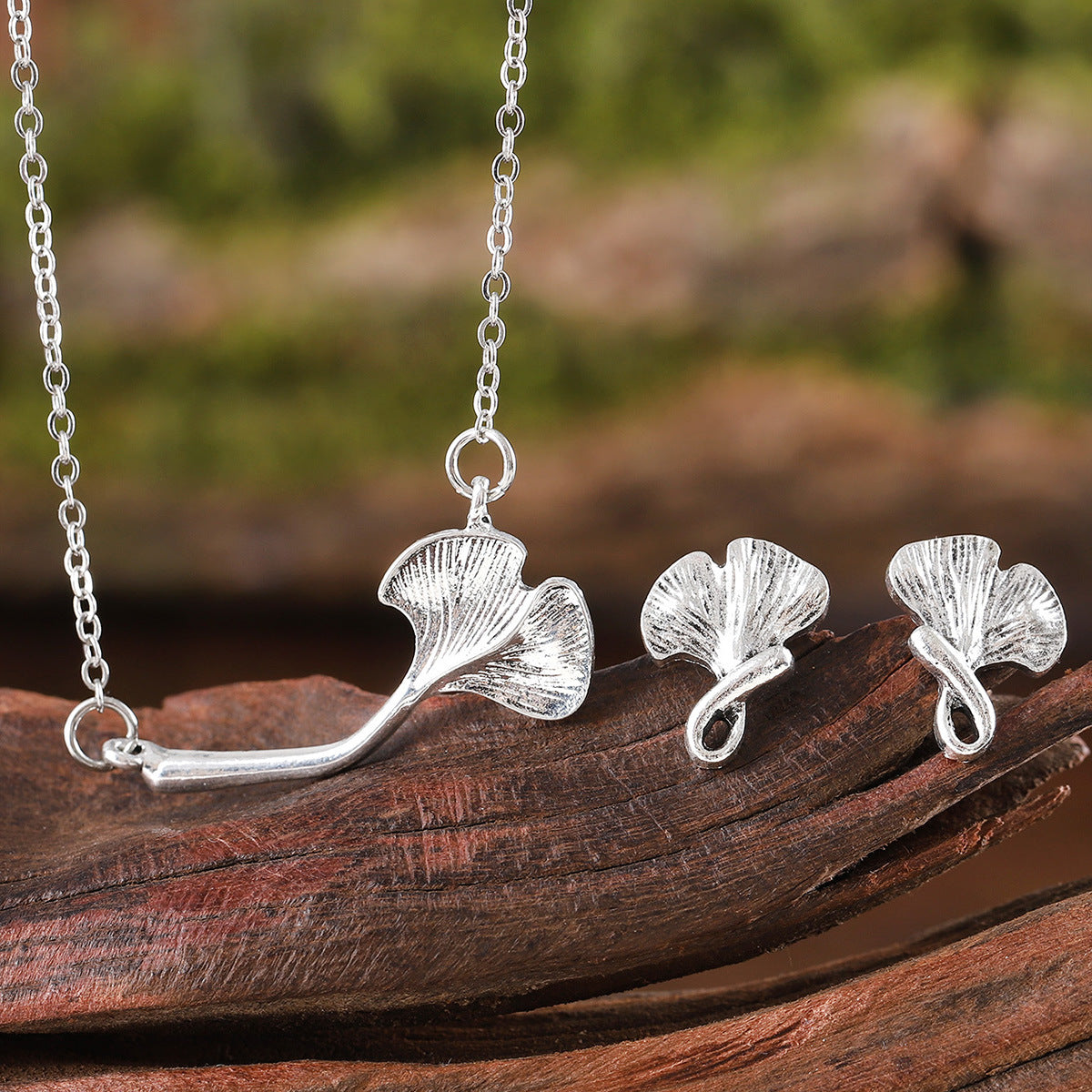 Silver ginkgo leaf necklace and earrings on a wooden surface with a natural background