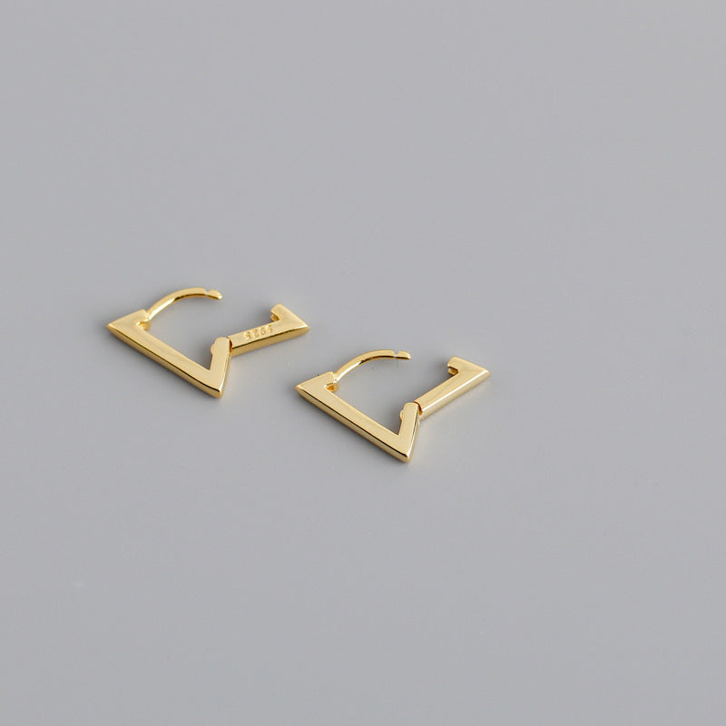 Gold geometric hoop earrings on a gray background