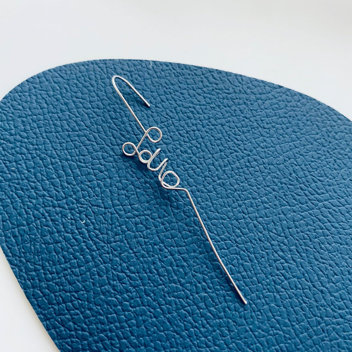 Silver hairpin with 'Lola' on a blue textured background