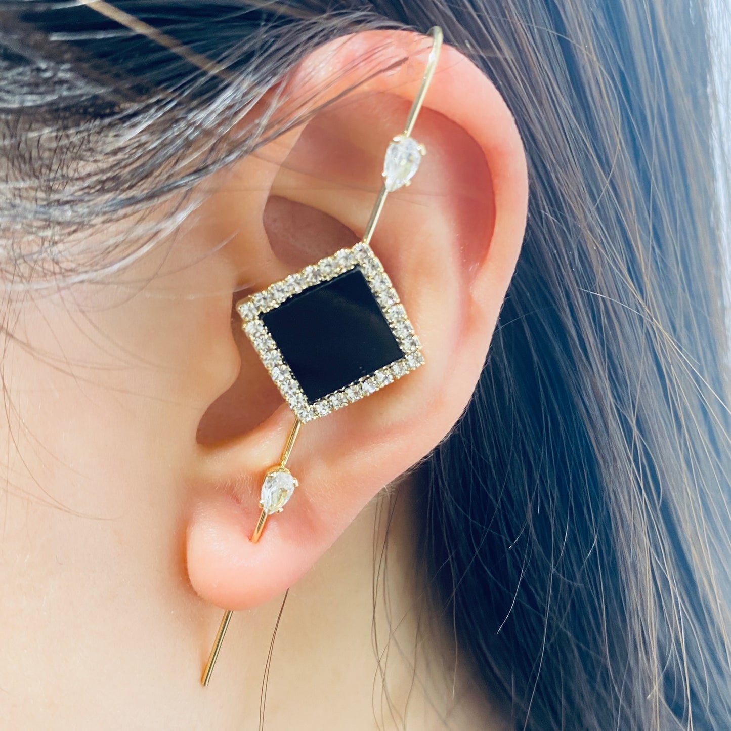 Close-up of an ear wearing a gold earring with a black gemstone and clear stones.