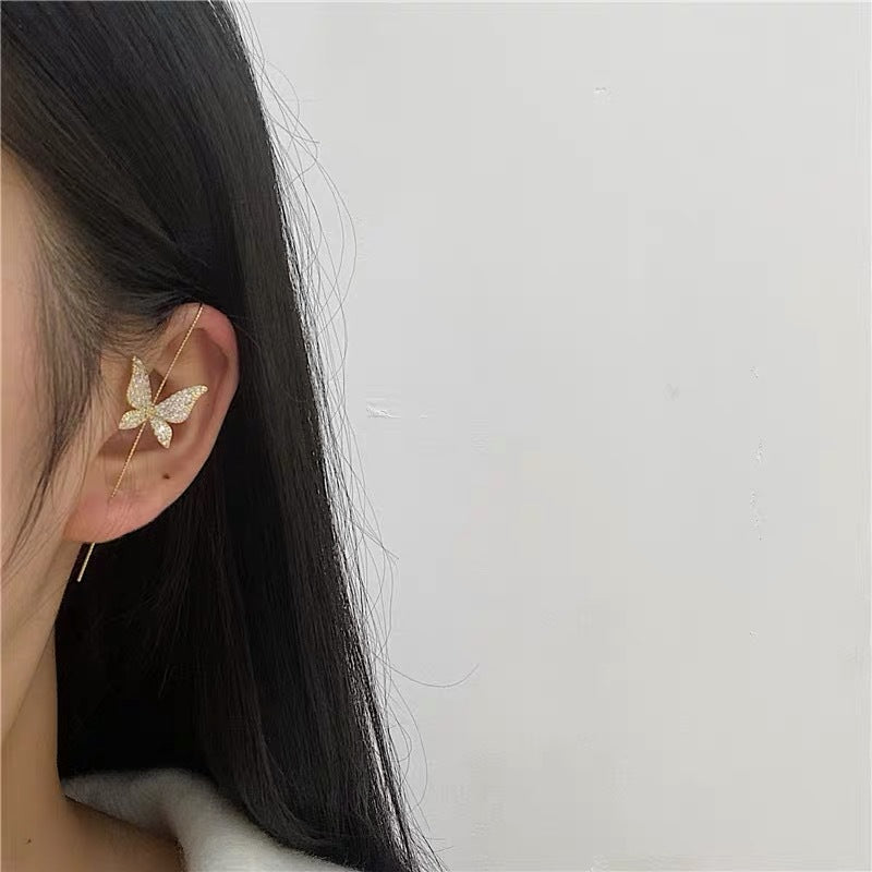 Butterfly-shaped earring worn by a person with dark hair on a light gray background
