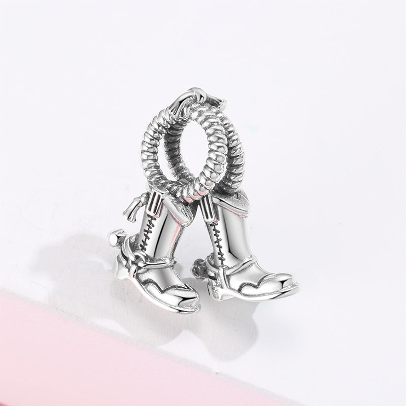 Silver charm with cowboy boot and spurs design on a light pink background