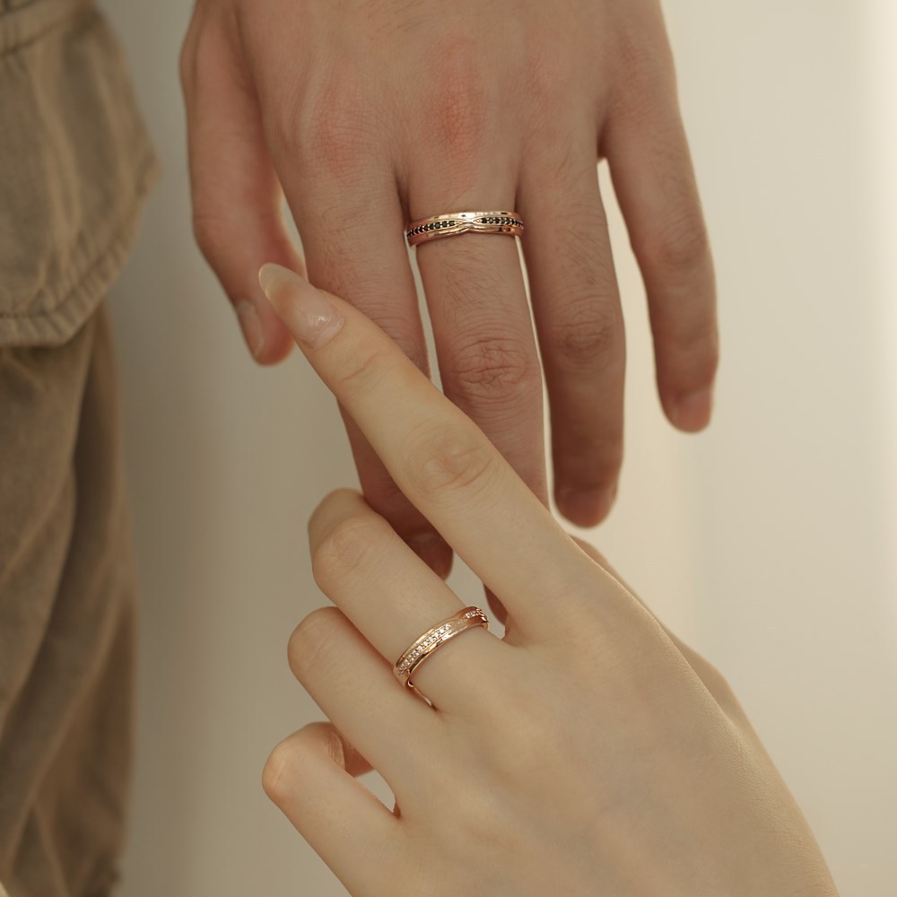Two hands wearing gold rings on a neutral background