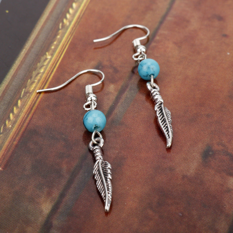 Silver feather and turquoise bead earrings on a textured surface