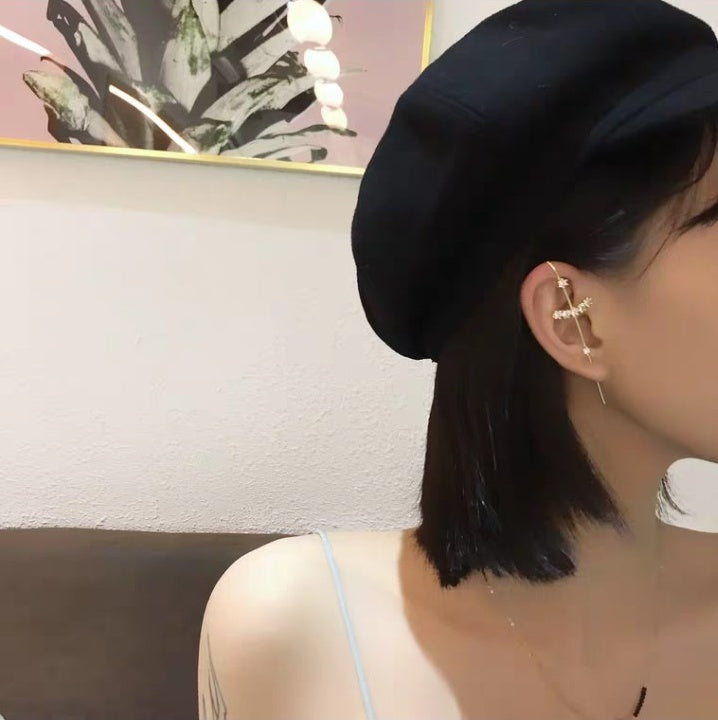 Close-up of a person wearing a gold earring with a cross design, sitting indoors.
