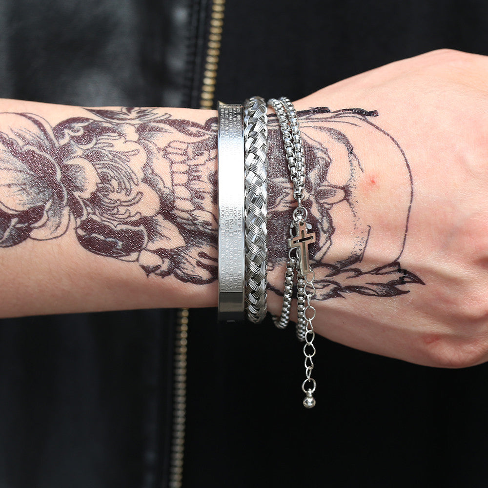 Close-up of a wrist with tattoos and multiple silver bracelets on a dark background