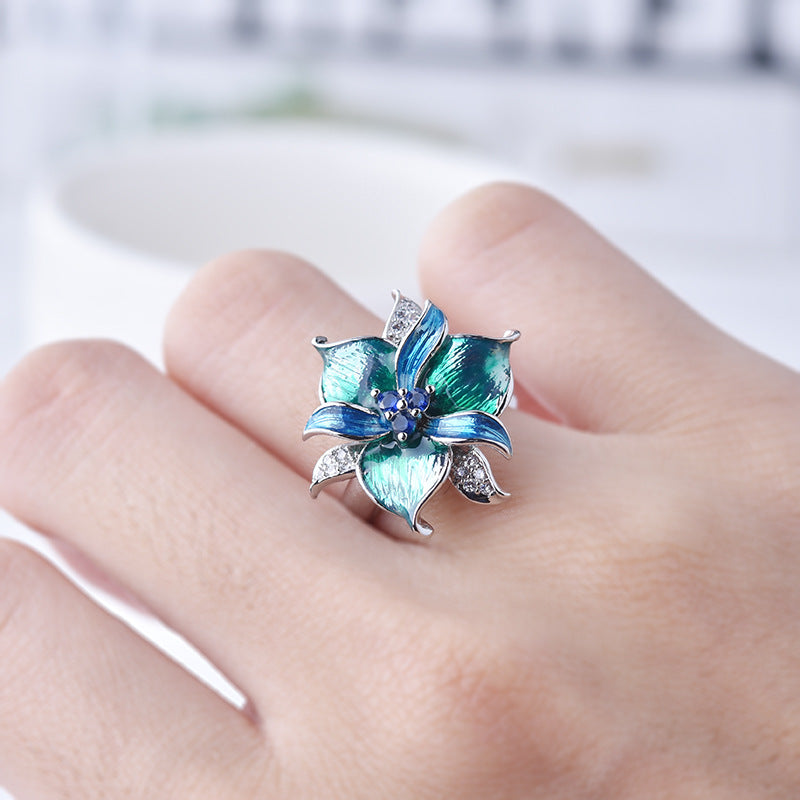 Blue flower-shaped earring on a hand with a blurred background