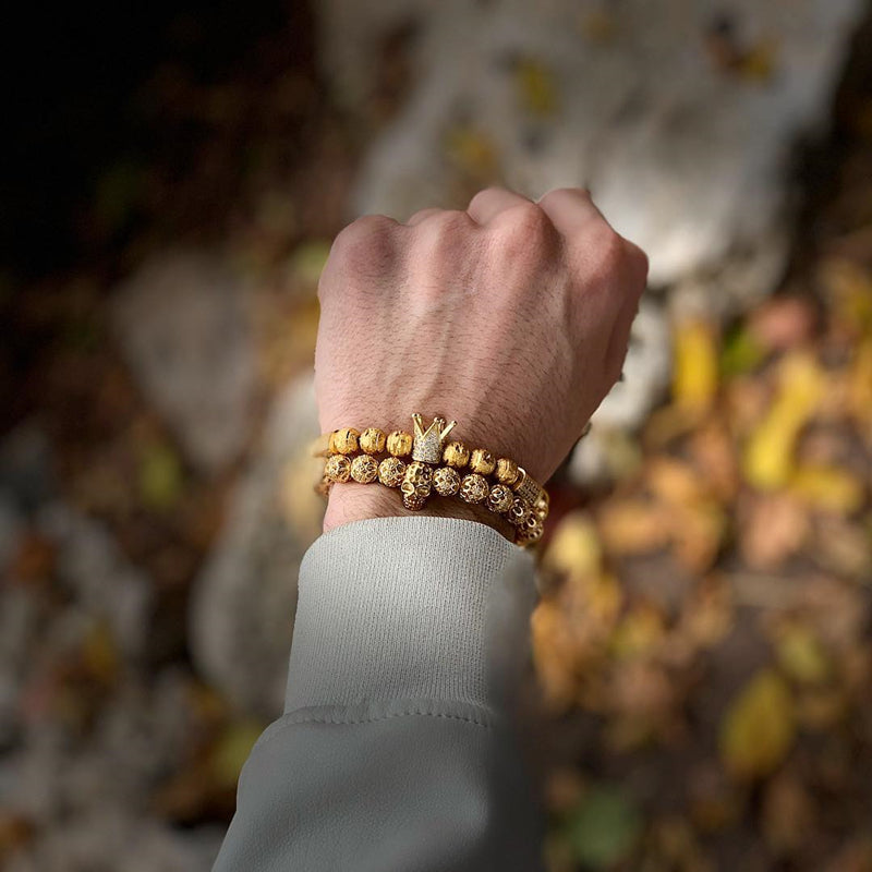 Hand wearing gold bracelets with a blurred natural background