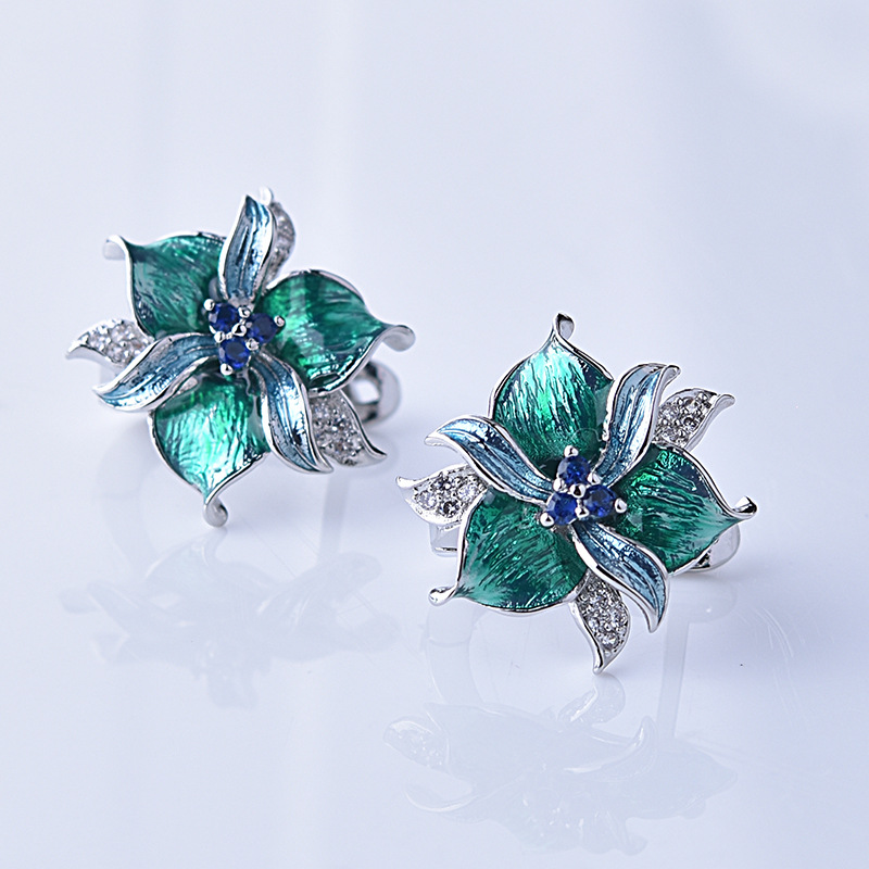 Pair of green floral earrings with blue centers on a light gray background
