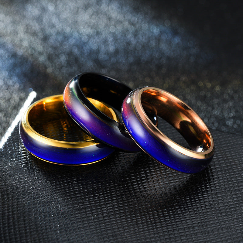 Three metallic rings in gold, blue, and bronze on a textured black surface