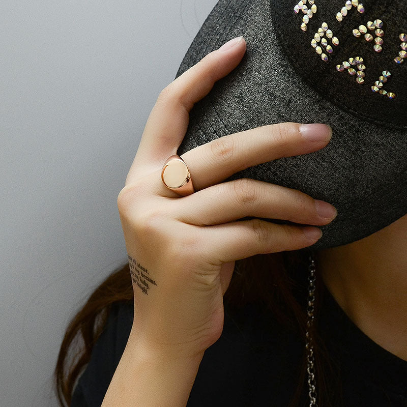 Hand wearing a gold ring holding a black textured bag with decorative elements.