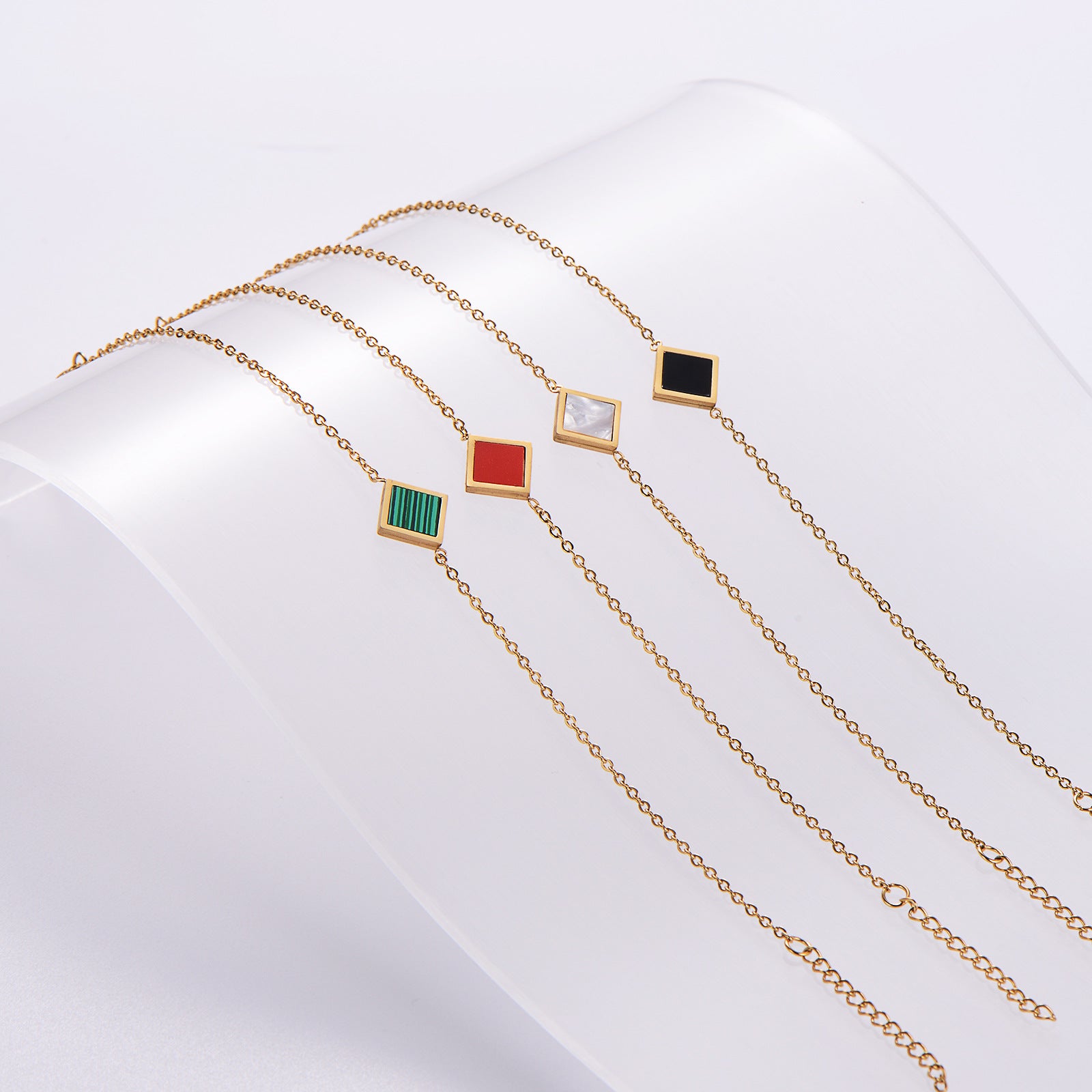 Gold necklaces with colorful square pendants on a white background