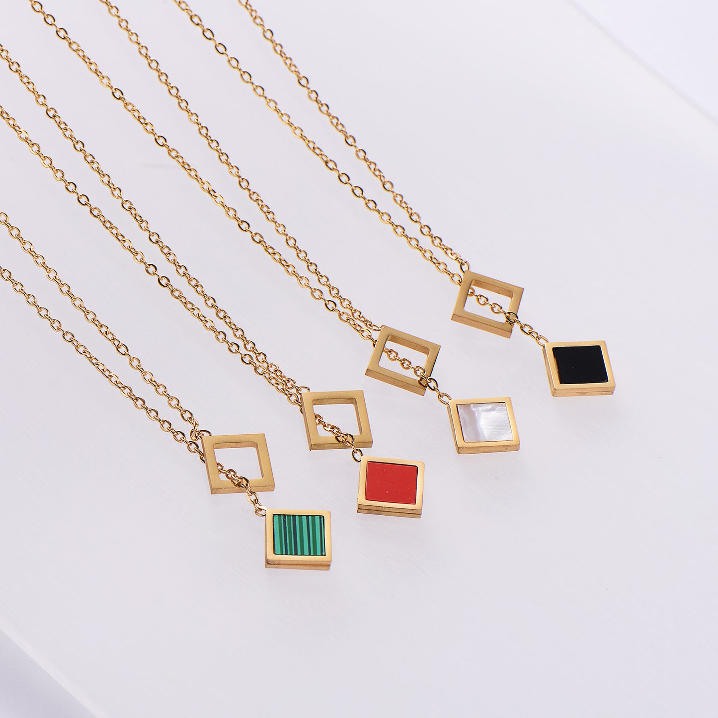 Gold necklaces with square pendants in various colors on a light gray background