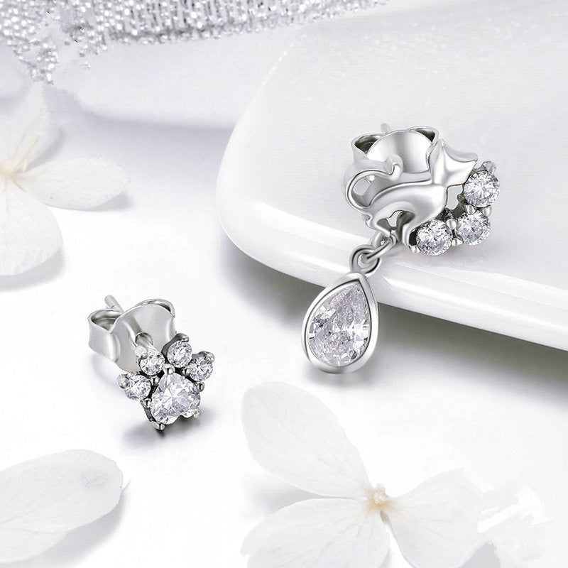 Silver earrings with clear gemstones on a white surface with flowers