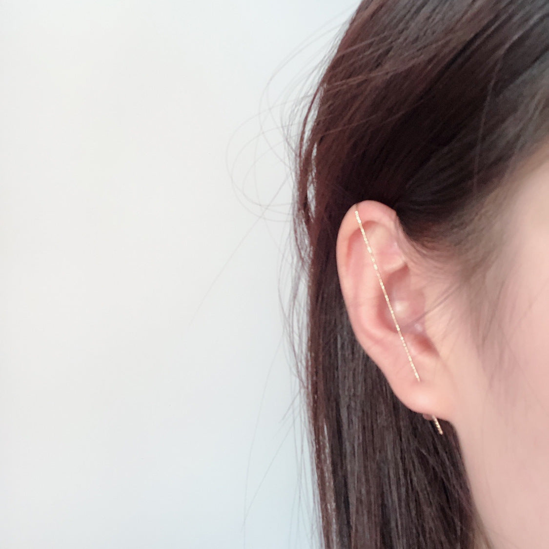 Gold ear cuff worn by a person with brown hair on a light gray background