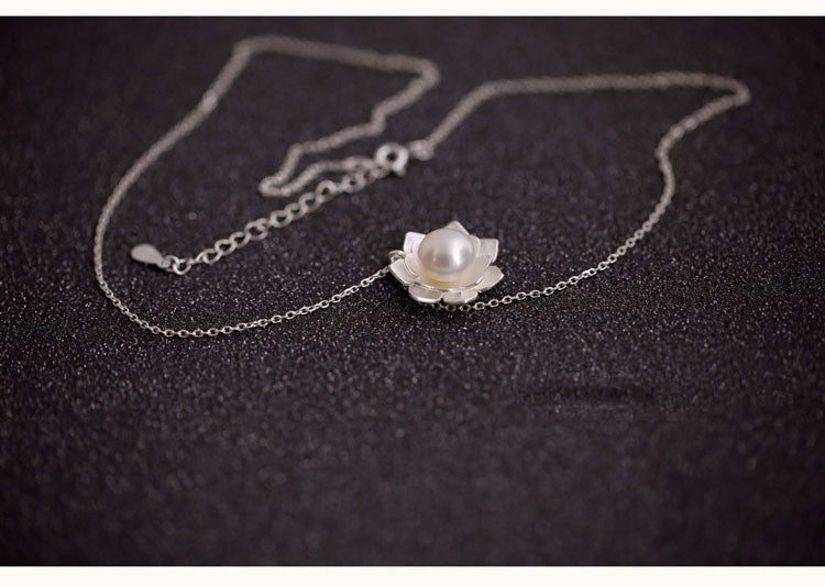 Silver necklace with a pearl pendant on a dark fabric background