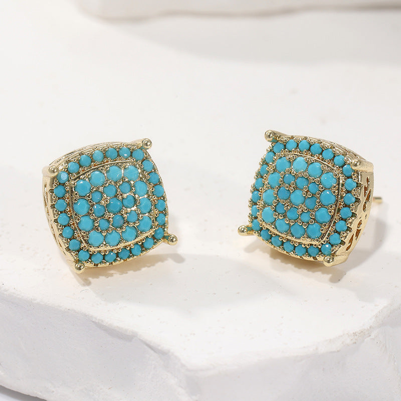 Pair of gold earrings with turquoise stones on a white cushion
