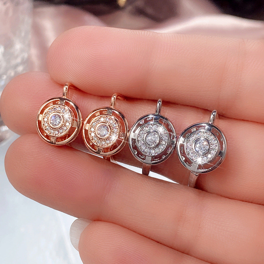Four diamond earrings held between fingers, showcasing gold and silver colors.