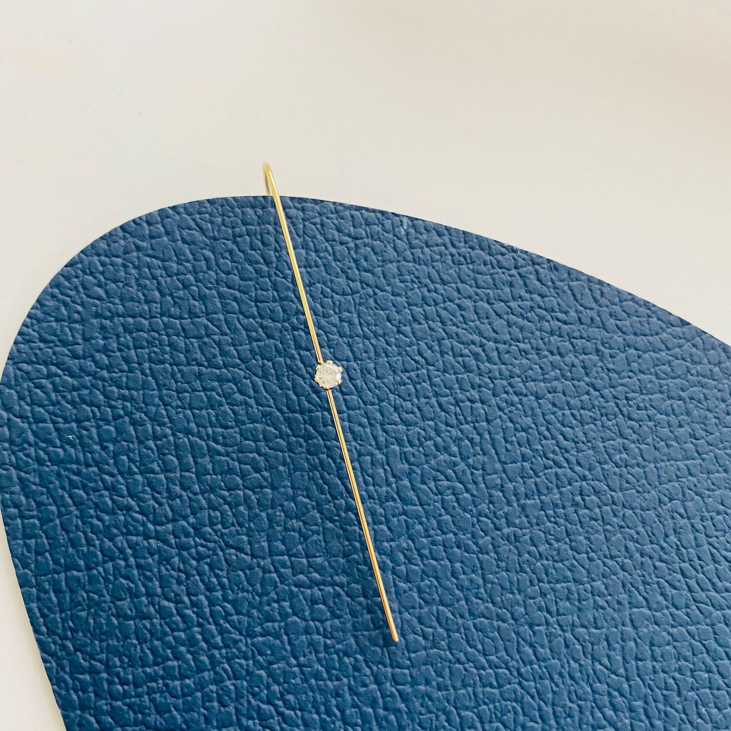 Gold necklace with a small pendant on a blue textured card