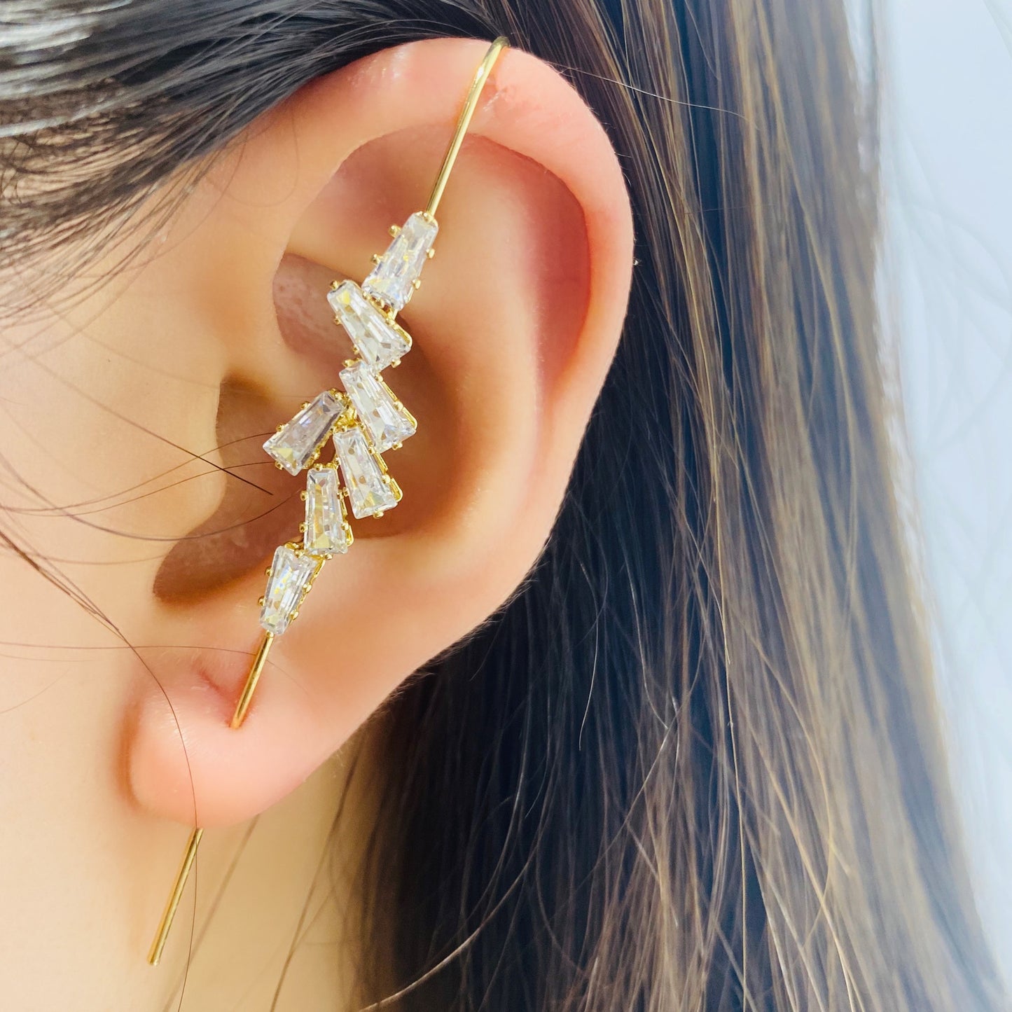 Gold earrings with clear stones worn by a person with dark hair.
