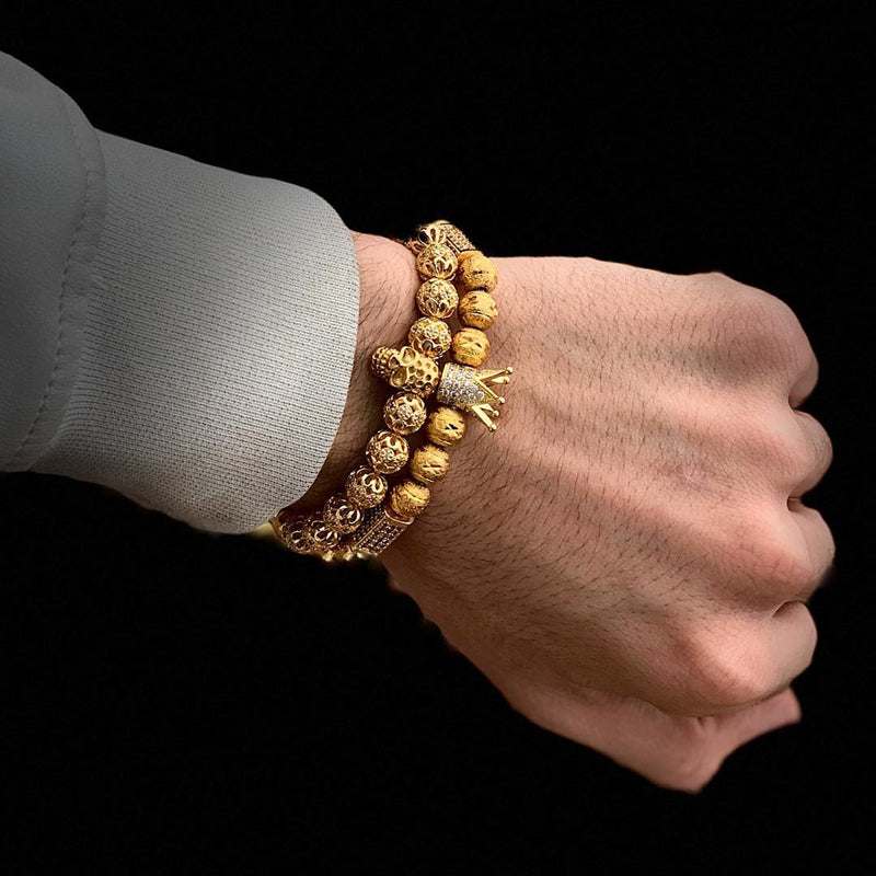 Hand wearing a gold beaded bracelet against a black background