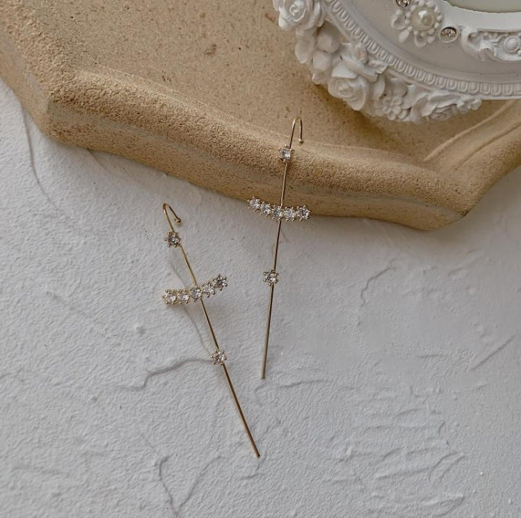 Two delicate gold earrings with small gemstones on a textured surface.