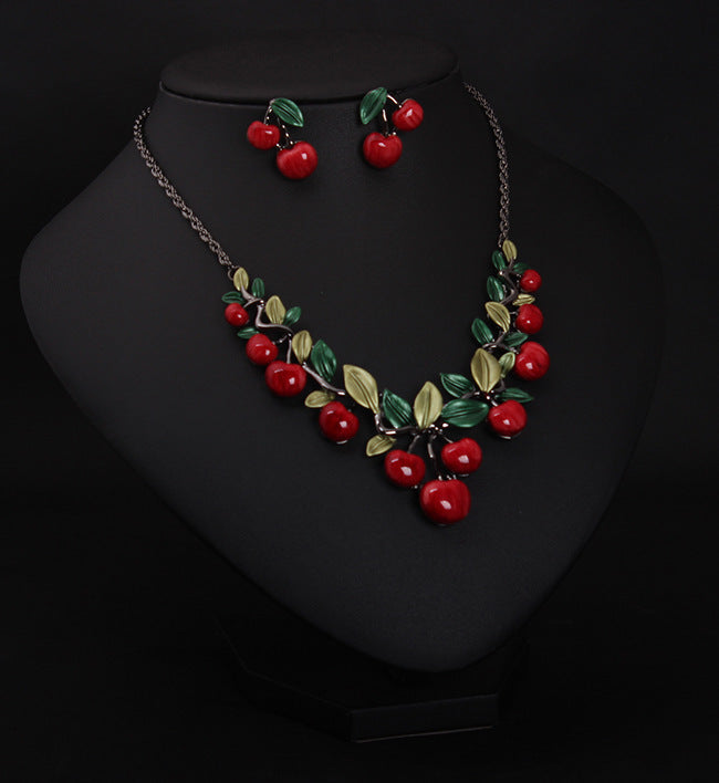 Jewelry set with necklace and earrings featuring red berries and green leaves on a black background