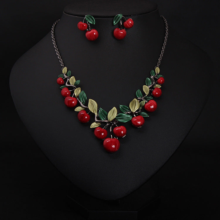 Necklace and earrings set with red cherries and green leaves on a black background