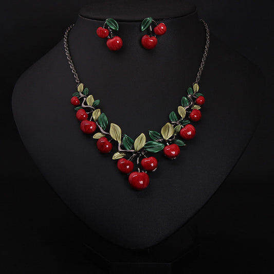 Necklace and earrings set with red cherries and green leaves on a black background
