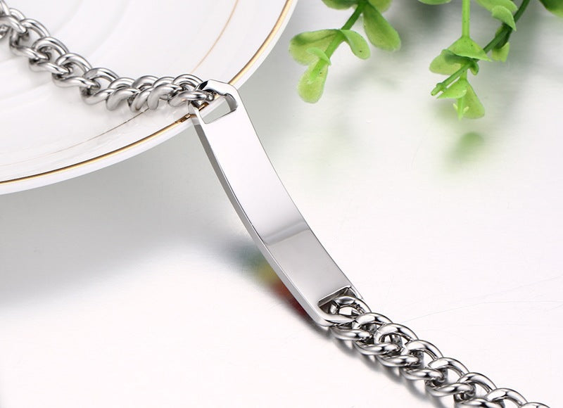 Silver chain with a rectangular tag on a white surface with green leaves in the background