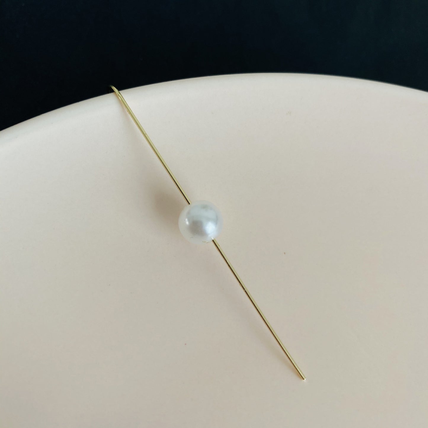 Single pearl on a thin gold rod against a dark background