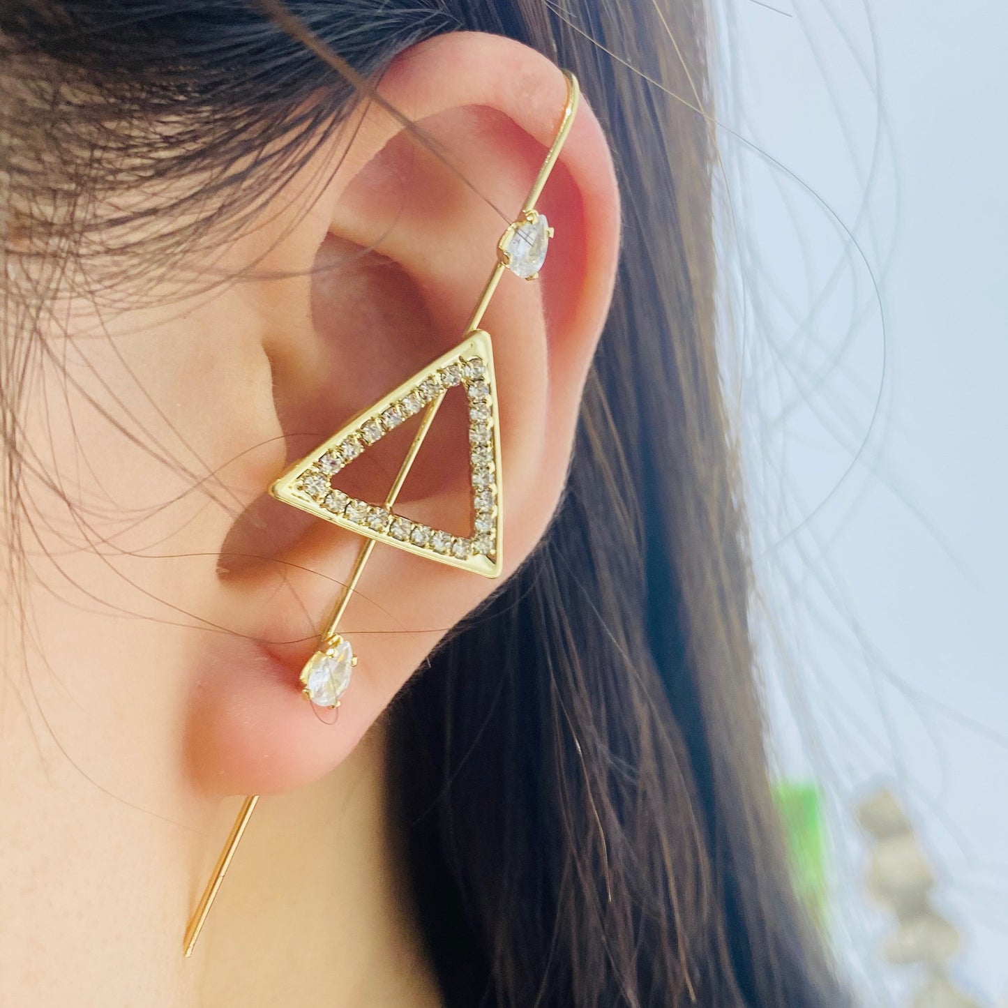 Gold triangle-shaped earring with clear stones worn by a person.