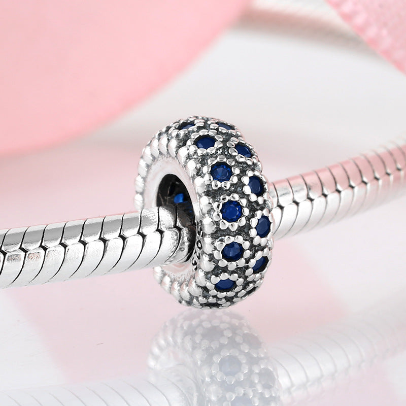 Silver charm with blue stones on a pink background