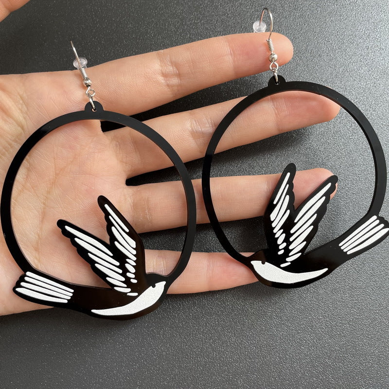 Black and white bird-shaped earrings held in a hand against a gray background